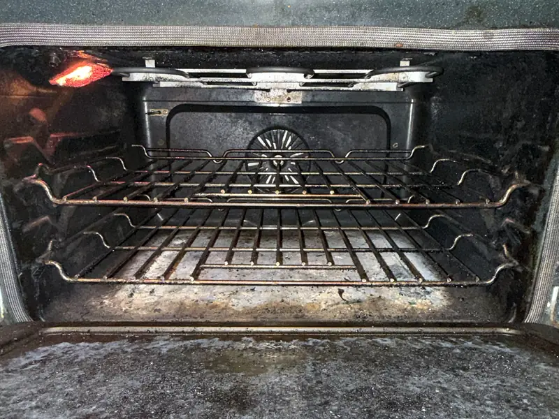 Oven interior coated in baked-on grease, white residue, and dirty racks before a move-out clean